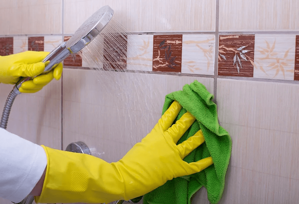 two hands of a man cleaning bathroom tiles